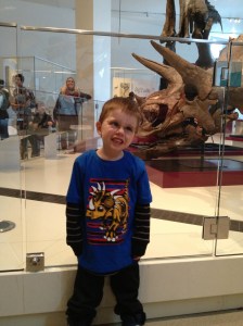 Aiden showing off his dinosaur face in front of a triceratops 