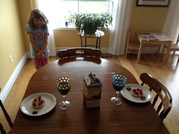 Uncooked English Muffin with raspberry smily face on top. Two broken granola bars on the sides for ears, and two big glasses of Chocolate Soya Milk. Excellent presentation.